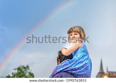 Little preschool girl sitting on shoulder of father. Happy toddler child and man observing rainbow on sky after summer rain. Happy family, bonding, love. Summertime. Dad and daughter. Father's day.