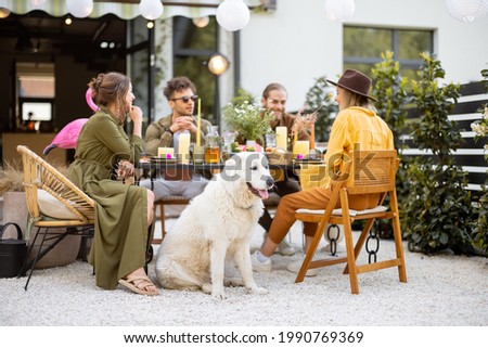 A group of young friends and dog have delicious dinner, having great summertime together at the backyard of the country house