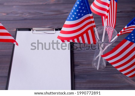 Top view clipboard with blank paper and US flags on grey wood.