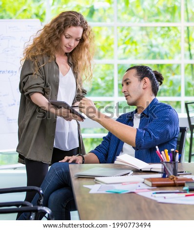 Focus handsome Caucasian male boss teaching, explaining, giving advice to hipster trendy creative female subordinate in comfortable modern office with profession and background of diverse staff