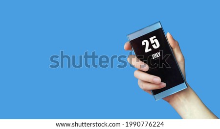july 25. 25th day of the month, calendar date.Woman's hand holds mobile phone with blank screen on blue isolated background. Summer month, day of the year concept.