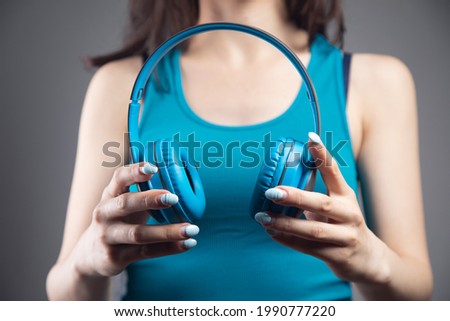 young woman holds large headphones on a gray background
