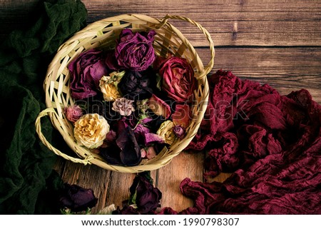Dried rose buds in a wicker basket with green and burgundy material on a background of wooden boards
