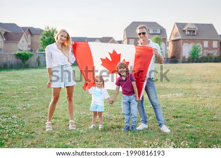Happy Canada Day. Caucasian family with kids boy and girl standing in park and holding large Canadian flag. Parents with kids children celebrating Canada Day on 1st of July outdoor. Royalty-Free Stock Photo #1990816193