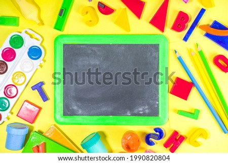 Back To School Concept. Various school stationery and supplies - chalk, color pencil, paints, notebooks, brushes, tablet, small blackboard. Flatlay top view copy space on yellow bright background. 