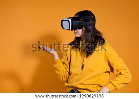 Immersion in cyberspace, virtual reality and the user. A young female gamer in a yellow hoodie and with a VR helmet on her head on a yellow background.