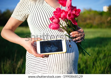 close-up photography. woman's hand holding an ultrasound scan on the background of a pregnant belly.