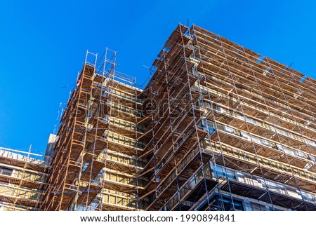 Scaffolding on the facade of a high-rise building under construction. Construction of multi-storey building. Unfinished house on background of blue sky.
