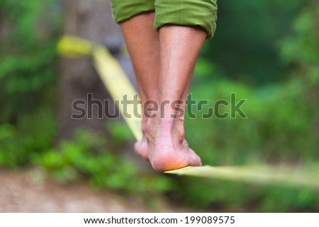 Slacklining is a practice in balance that typically uses nylon or polyester webbing tensioned between two anchor points. Royalty-Free Stock Photo #199089575