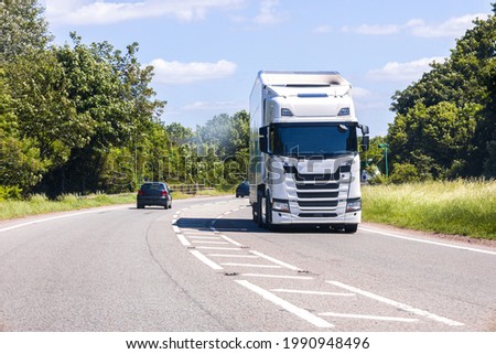 A large HGV vehicle traveling along one of the main road routes of the United Kingdom, on a summer's day. Taking goods to and from their suppliers and customers. Royalty-Free Stock Photo #1990948496