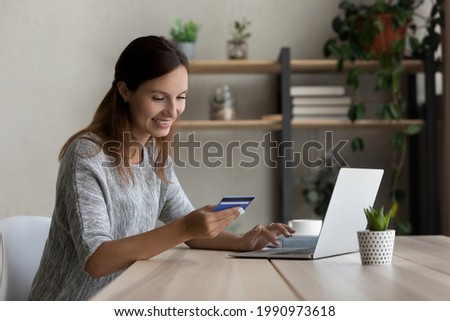 Happy woman holding plastic credit card, using laptop, paying online, smiling satisfied young female customer making secure internet payment, entering information, typing, browsing banking service