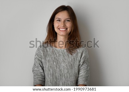 Head shot portrait of positive beautiful woman posing on grey studio background isolated, happy young female with healthy toothy smile and perfect smooth skin looking at camera, natural beauty