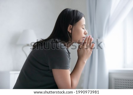 Peaceful mixed raced girl with closed eyes praying to god, keeping hands together in begging, asking lord for help or thanking for luck. Spirituality, religion, faith, worship concept. Side view