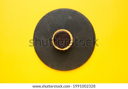 A picture of chocolate tart serve on slate plate and yellow background.