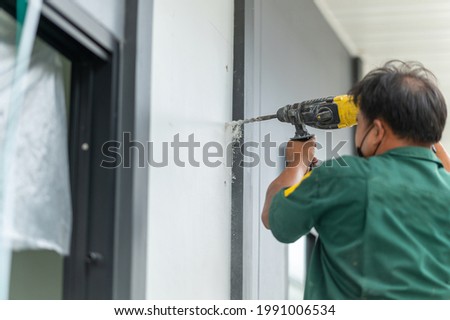Construction workers using an electric drill to drill holes to the wall at home.