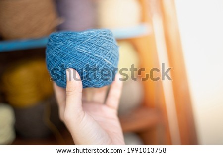 Female hand holding the dark blue yarn ball with the earth tone yarn in the wooden cupboard prepare for made Crochet and knitting. For leisure concept.