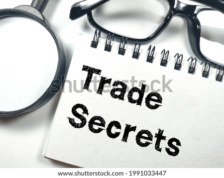 Business concept.Text TRADE SECRETS on notebook with magnifying glass and glasses on white background.