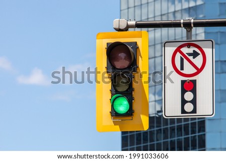 A No Right Turn On Red pictograph sign next to a traffic signal showing a green go light Royalty-Free Stock Photo #1991033606
