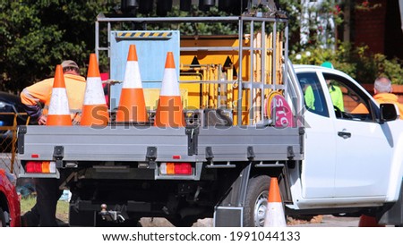 Road work company ute loaded with signs and orange road cones. Road workers are in the background