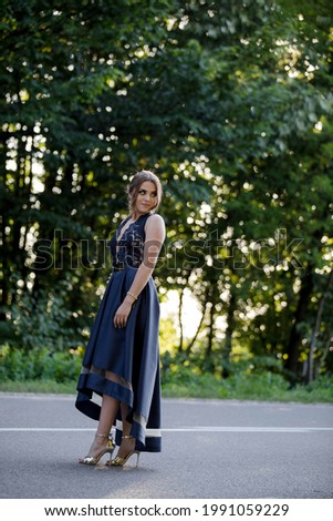 An attractive Caucasian female wearing an elegant dark blue dress posing in a park