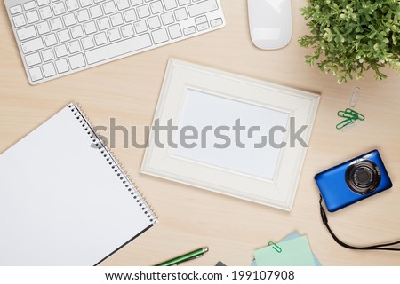 Photo frame on office table with notepad, computer and camera. View from above