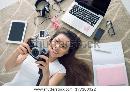 Cheerful Vietnamese girl lying on the floor  with her camera in hands Royalty-Free Stock Photo #199108322