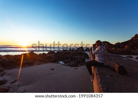 A female photographer taking pictures of the sea at sunset