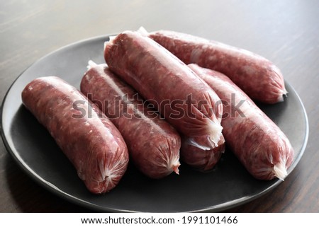 Raw beef sausages on a black plate.