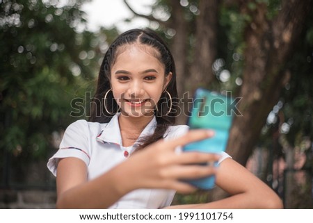 A pretty vain young asian woman in a student uniform takes a selfie of herself while at the park. Taking a photo for social media.