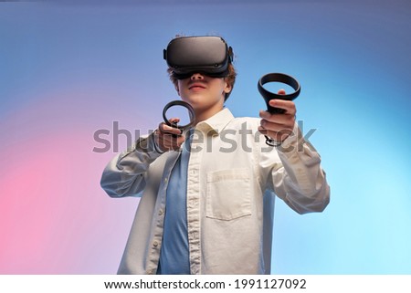 young boy play VR games in virtual reality helmets on bright colourful background, hold controllers and look away. guy in VR helmets play video games. Isolated. VR gaming concept