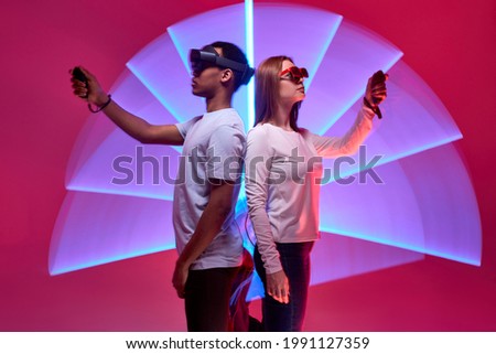 Friends in VR helmets compete in virtual reality game. Two gamers in virtual reality helmets play VR games, isolated in studio on colourful background, hold controllers. gaming, leisure with friends