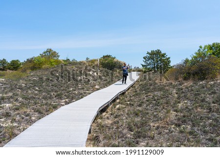 A man on a wooden walkway takes pictures of the sand dunes using his phone. Plum Island on the northeast coast of Massachusetts. A place for nesting birds
