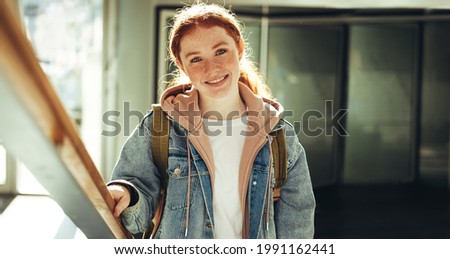 Happy young woman standing in college. Female student in casual clothing smiling at camera in college.
