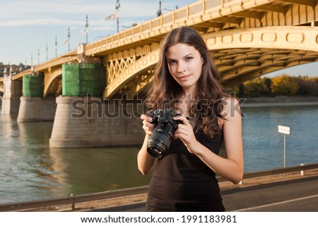 Outdoors portrait of young brunette tourist woman taking photos of the city.