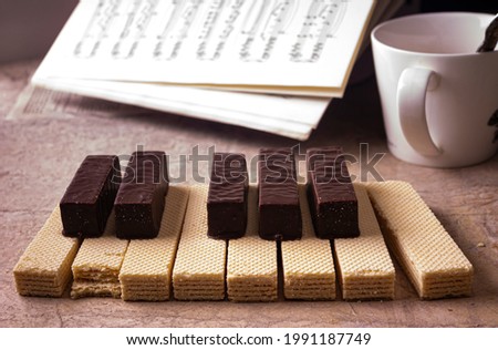 Piano keyboard made of waffles and marshmallows in chocolate, a cup of tea, notes in the background.
