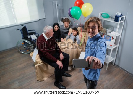 A family taking a selfie at the hospital room with a birthday girl lying in bed, everyone is making funny faces