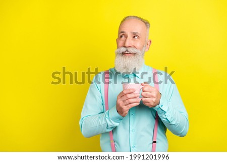 Photo of cheerful elder man hold cup look empty space wear blue shirt isolated on vibrant yellow color background