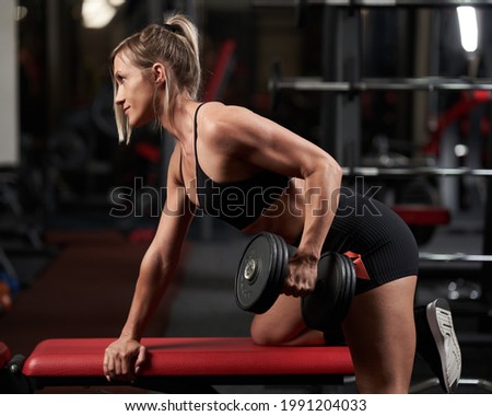 Fitness woman doing dumbbell row for back workout on a bench in the gym
