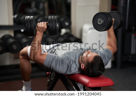 Young fitness man doing bench press with heavy dumbbells for chest workout Royalty-Free Stock Photo #1991204045