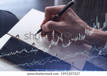 A trader in formal wear writing down some quotes to research stock market trends using smart phone for right investment solutions. Wealth management concept. Hologram Forex chart over close up shot.