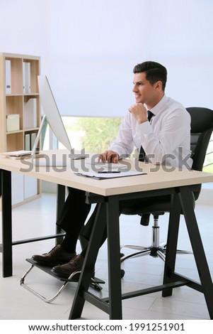 Man using footrest while working on computer in office Royalty-Free Stock Photo #1991251901