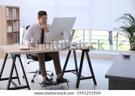 Man using footrest while working on computer in office Royalty-Free Stock Photo #1991251904