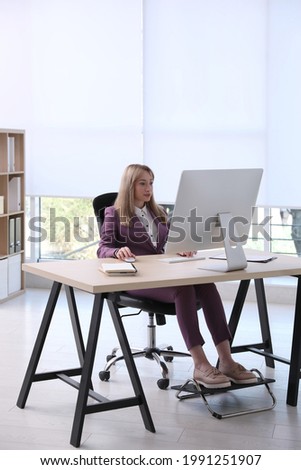 Woman using footrest while working on computer in office Royalty-Free Stock Photo #1991251907