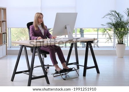 Woman using footrest while working on computer in office Royalty-Free Stock Photo #1991251910