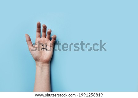 A hand with a picture of a sad face. A symbol of depression and psychological trauma in humans
