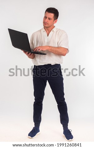 Young businessman with laptops. Vertical portrait of businessman. Man in white shirt is holding computer. Guy is using laptop while standing. Man is typing something. Business portrait with computer