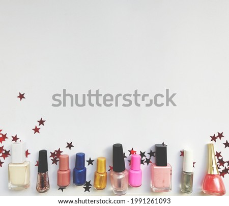 Overhead view of lots of vivid different nail polishes surrounded by lots of small white red stars on white background with space for text 
