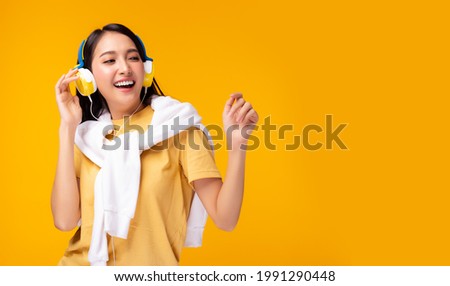 Happy beautiful asian young woman listening music in headphones and singing on yellow background in excitement Beautiful young girl dancing She looking at copy space Expressive facial expressions Royalty-Free Stock Photo #1991290448
