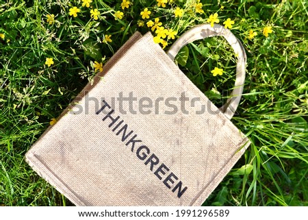 jute bag with inscription THINK GREEN and green leaf on grass with yellow flower. Eco friendly, zero waste,no plastic concept. top view.