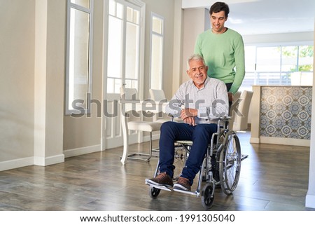 Satisfied senior citizen in a wheelchair looked after by his son in home care or in a retirement home Royalty-Free Stock Photo #1991305040